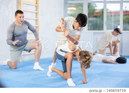 Diligent preteen student twisting his opponent's arm in sports hall Diligent preteen student twisting his opponent's arm in sports hall 140659739