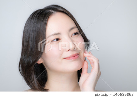 白背景で透明感で美肌に触れるカメラ目線の笑顔の女性スキンケアと美容クローズアップイメージ 白背景で透明感で美肌に触れるカメラ目線の笑顔の女性スキンケアと美容クローズアップイメージ 140659868