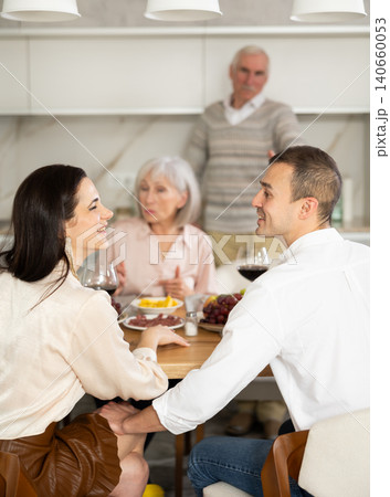 Young couple flirting sitting around table together with old family members looking with objection Young couple flirting sitting around table together with old family members looking with objection 140660053