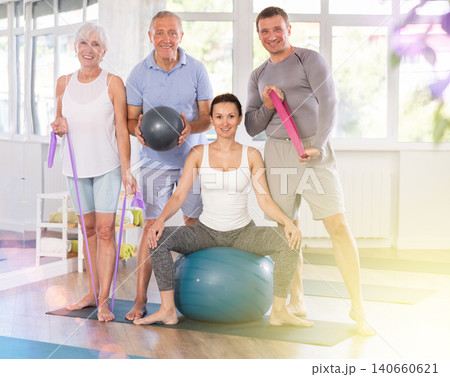 Group of women and men of different ages in sportswear with fitness balls and resistance bands posing together in sports studio, ready for training 140660621