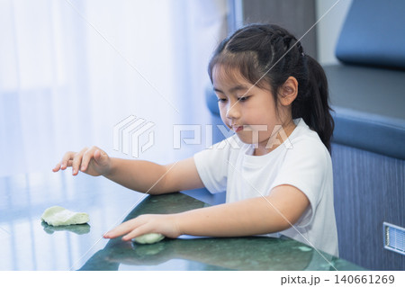Young girl in casual clothing concentrating while playing with slime on a table in a modern room with curtains and a blue chair in the background 140661269