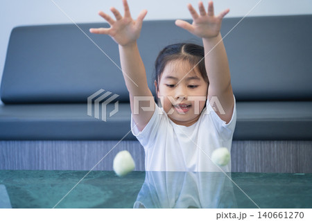 Young Asian girl playing with tennis balls at home, smiling and having fun during a casual indoor activity in a modern living room setting Young Asian girl playing with tennis balls at home, smiling and having fun during a casual indoor activity in a modern living room setting 140661270