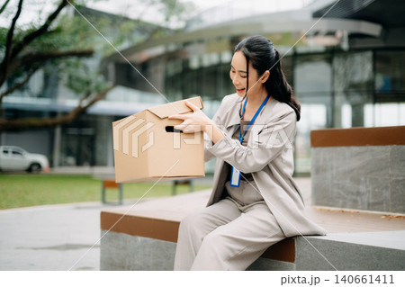 Businesswoman carrying box after job loss, representing layoff, unemployment, career transition, and corporate crisis Businesswoman carrying box after job loss, representing layoff, unemployment, career transition, and corporate crisis 140661411