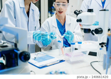Team of scientists analyzing blue liquid samples in a modern lab, showcasing biotechnology, chemistry, and medical research Team of scientists analyzing blue liquid samples in a modern lab, showcasing biotechnology, chemistry, and medical research 140661420