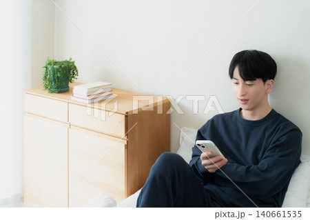 ベッドでスマホを見る若い男性 140661535