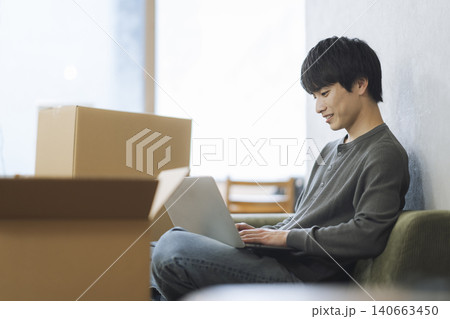 段ボール箱に囲まれて座りノートパソコンで作業をする若い男性 引っ越し イメージ 段ボール箱に囲まれて座りノートパソコンで作業をする若い男性 引っ越し イメージ 140663450