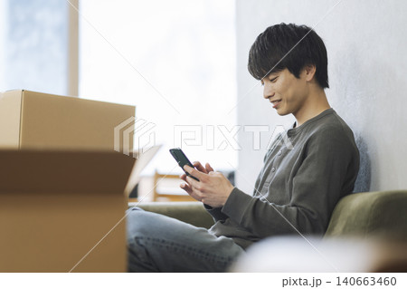 段ボール箱に囲まれてスマートフォンを操作する若い男性 引っ越し イメージ 段ボール箱に囲まれてスマートフォンを操作する若い男性 引っ越し イメージ 140663460