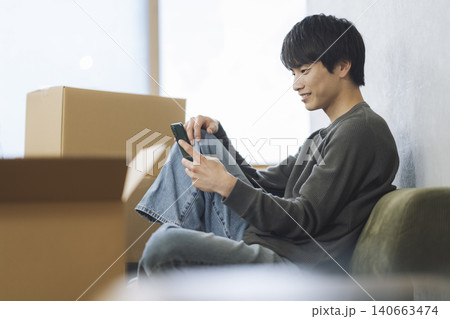 段ボール箱に囲まれてスマートフォンを操作する若い男性　引っ越し　イメージ 140663474