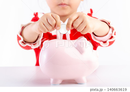 Little Asian girl putting a coin into a pink piggy bank, concept of saving money and financial education for kids. 140663619