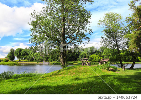 Outside seating area with wooden benches near to lake. Beautiful landscape with river, benches and green space. Europe. Picturesque landscape and leisure area for recreation and relaxation Outside seating area with wooden benches near to lake. Beautiful landscape with river, benches and green space. Europe. Picturesque landscape and leisure area for recreation and relaxation 140663724