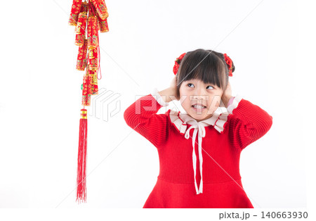Cute Asian girl in red dress holding firecracker decorations and smiling, Chinese New Year celebration concept. Cute Asian girl in red dress holding firecracker decorations and smiling, Chinese New Year celebration concept. 140663930