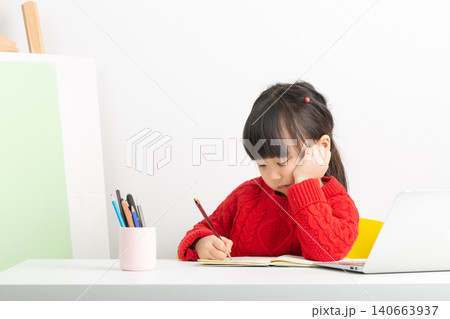 A bright and focused Asian girl is doing her homework at her desk, her expression one of deep thought. A bright and focused Asian girl is doing her homework at her desk, her expression one of deep thought. 140663937