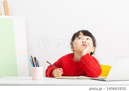A bright and focused Asian girl is doing her homework at her desk, her expression one of deep thought. 140663938