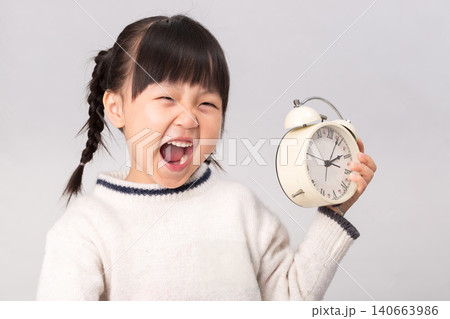 Smiling Asian child holding a white alarm clock, concept of time management, punctuality or waking up early. 140663986