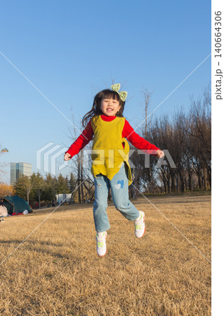 a jumping happy little girl in a yellow vest and red sweater in the park. 140664306