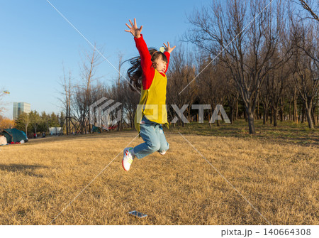 a jumping happy little girl in a yellow vest and red sweater in the park. 140664308