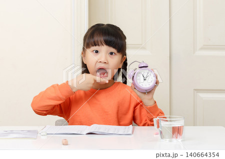 A surprised Asian little girl points to the alarm clock, seemingly expressing the concept of being late or time pressure. A surprised Asian little girl points to the alarm clock, seemingly expressing the concept of being late or time pressure. 140664354