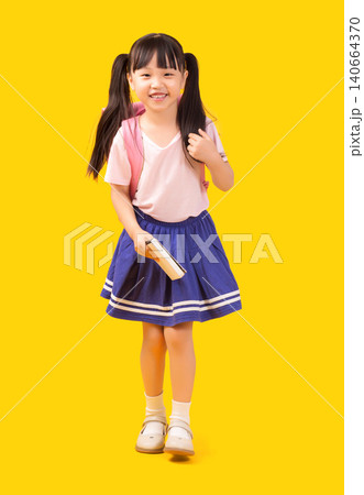 Friendly young Asian girl in school uniform  with pink backpack and holding notebook on yellow background 140664370