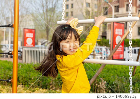 Joyful little girl smiles excitedly while playing inside a rope climbing net at an outdoor playground. Joyful little girl smiles excitedly while playing inside a rope climbing net at an outdoor playground. 140665218