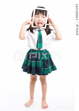 Playful Asian girl in school uniform looking through a white frame making a funny face. Playful Asian girl in school uniform looking through a white frame making a funny face. 140665263