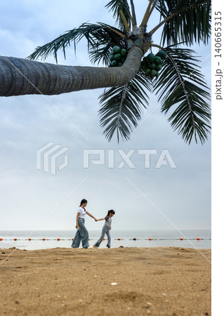 Two girls walking on beach under coconut palm tree, summer vacation and friendship concept Two girls walking on beach under coconut palm tree, summer vacation and friendship concept 140665315