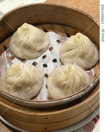 Steamed xiaolongbao dumplings with delicate thin skin, slightly translucent top folds, and savory soup filling inside, highlighting their soft texture and freshly steamed appearance in close-up detail Steamed xiaolongbao dumplings with delicate thin skin, slightly translucent top folds, and savory soup filling inside, highlighting their soft texture and freshly steamed appearance in close-up detail 140665468