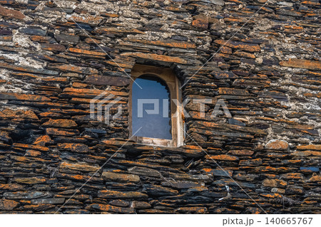 Ancient stone wall, weathered and textured with small arched window 140665767