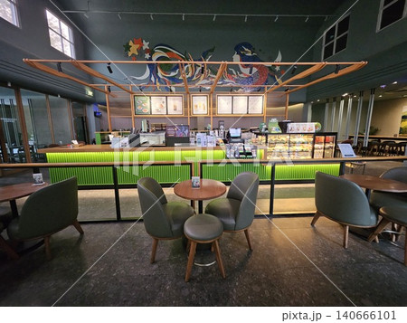 Modern coffee shop interior featuring a vibrant illuminated green service counter, stylish wooden bar. 140666101