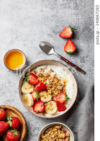 Natural  Greek yogurt with granola, banana and strawberries in a bowl on a concrete  background 140667265