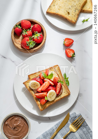 Toasted bread with chocolate cream, strawberries, and banana on a plate on a marble background Toasted bread with chocolate cream, strawberries, and banana on a plate on a marble background 140667266