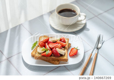 Toasted bread with chocolate cream, strawberries, and banana on a plate on a tile background Toasted bread with chocolate cream, strawberries, and banana on a plate on a tile background 140667269