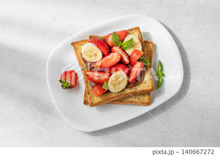 Toasted bread with chocolate cream, strawberries, and banana on a plate on a concrete background 140667272