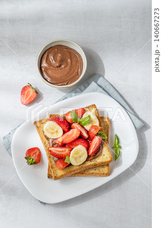 Toasted bread with chocolate cream, strawberries, and banana on a plate on a concrete background Toasted bread with chocolate cream, strawberries, and banana on a plate on a concrete background 140667273