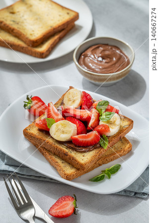 Toasted bread with chocolate cream, strawberries, and banana on a plate on a concrete background 140667274