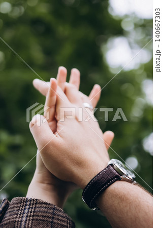 Hands holding together with wrist watch on blurred green tree background. Vertical close up of couple holding hands, male and female touch, love, relationship and wedding concept Hands holding together with wrist watch on blurred green tree background. Vertical close up of couple holding hands, male and female touch, love, relationship and wedding concept 140667303