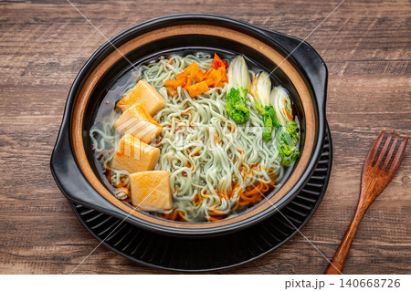 Traditional Chinese green spinach noodles with fish tofu served in a rustic black clay pot 140668726