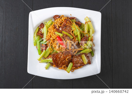 Savory stir-fried noodles with tender sliced beef and crisp green celery on a white plate Savory stir-fried noodles with tender sliced beef and crisp green celery on a white plate 140668742