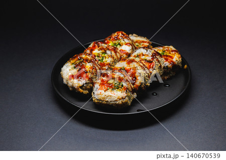 Delicious sushi rolls served on a black plate with sauce drizzled on top captured in low light setting Delicious sushi rolls served on a black plate with sauce drizzled on top captured in low light setting 140670539