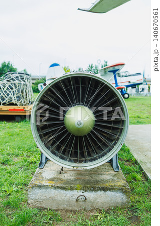 Jet engine sits on a concrete pad at an outdoor aviation display in the daytime with green grass and other aircraft in the background 140670561