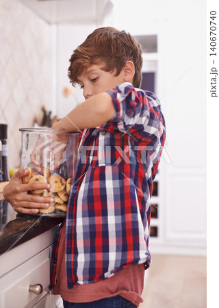 Hungry, naughty and boy in kitchen with cookie jar for hunger, snack or sweet treats at home. Biscuit, food and sneaky young teen kid in apartment with glass container reaching for baked goods 140670740