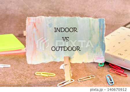 A sign with the words indoor vs outdoor is displayed on a table. The table has colorful sticky notes, paper clips, and a calculator nearby A sign with the words indoor vs outdoor is displayed on a table. The table has colorful sticky notes, paper clips, and a calculator nearby 140670912