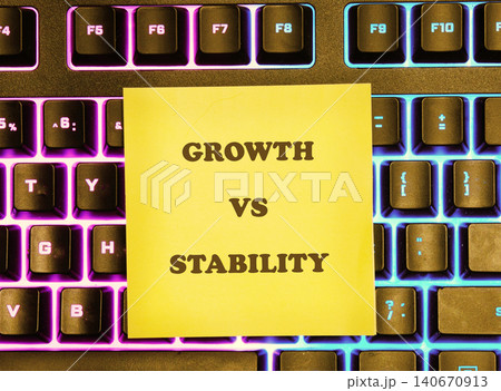 A yellow sticky note shows the words growth and stability. It is placed on a computer keyboard with colorful backlighting. The keyboard has various keys visible A yellow sticky note shows the words growth and stability. It is placed on a computer keyboard with colorful backlighting. The keyboard has various keys visible 140670913