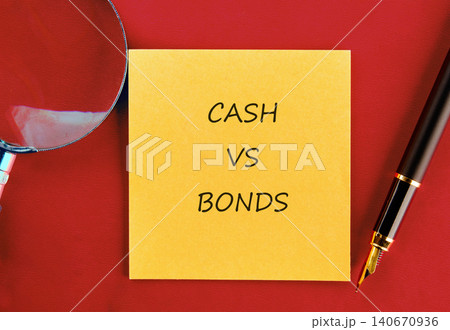 A yellow sticky note shows the words cash vs bonds on a red surface. A pen and a magnifying glass are nearby. This setup suggests a study on financial topics A yellow sticky note shows the words cash vs bonds on a red surface. A pen and a magnifying glass are nearby. This setup suggests a study on financial topics 140670936