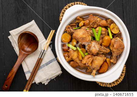 chinese traditional braised chicken with chestnuts in a white ceramic casserole pot, flat lay on dark wooden table with wooden spoon. chinese traditional braised chicken with chestnuts in a white ceramic casserole pot, flat lay on dark wooden table with wooden spoon. 140671655