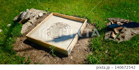 Concrete slab foundation with circular imprint surrounded by grass and debris, wooden frame visible, indicating preparation for construction or landscaping project Concrete slab foundation with circular imprint surrounded by grass and debris, wooden frame visible, indicating preparation for construction or landscaping project 140672542