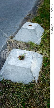 Concrete roadside barriers with grass growing through holes, positioned along a paved road with visible asphalt and surrounding vegetation Concrete roadside barriers with grass growing through holes, positioned along a paved road with visible asphalt and surrounding vegetation 140672557