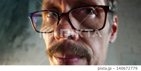 Middle-aged man with glasses and a mustache gazes directly at the camera, showcasing a close-up view of his facial features against a textured background Middle-aged man with glasses and a mustache gazes directly at the camera, showcasing a close-up view of his facial features against a textured background 140672779