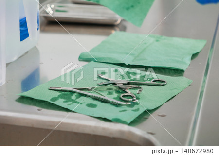 Sterile metal surgical instruments placed on green absorbent paper towels on a metallic table, representing professional preparation for medical procedures in a clinical setting Sterile metal surgical instruments placed on green absorbent paper towels on a metallic table, representing professional preparation for medical procedures in a clinical setting 140672980