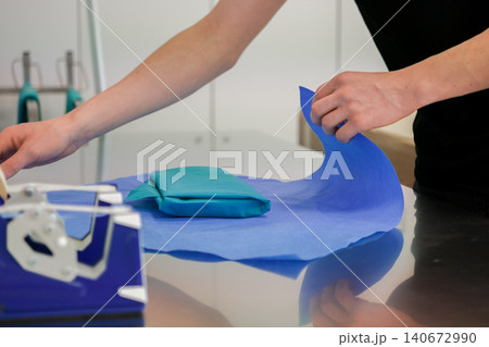 Medical professional hands wrapping sterile surgical equipment in blue protective paper, ensuring proper hospital equipment sterilization standards for a safe clinical surgery procedure Medical professional hands wrapping sterile surgical equipment in blue protective paper, ensuring proper hospital equipment sterilization standards for a safe clinical surgery procedure 140672990