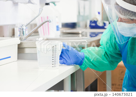 Medical professional wearing protective gear holds a plastic beaker in a sterile laboratory setting, demonstrating clinical precision during a controlled scientific research procedure 140673021